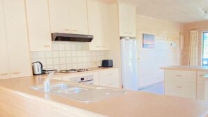 A modern kitchen with white cabinetry, a stainless steel sink, and a built-in oven. - Surfs Up on Surf Parade (Inverloch)