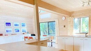 A spacious kitchen with a large island, wooden cabinets, and a dining area with chairs. - Surfs Up on Surf Parade (Inverloch)