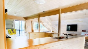 A modern kitchen with wooden cabinetry, a central island with a sink, and a staircase leading to an upper level. - Surfs Up on Surf Parade (Inverloch)