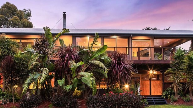 Una casa moderna con techo plano, grandes ventanales y un jardín cuidado con diversas plantas.
