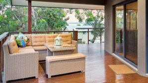 Un patio moderno al aire libre con mobiliario de mimbre, una mesa de vidrio y vistas a una casa y árboles.