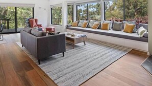 Un salón moderno con sofá, mesa de centro y ventanas amplias que ofrecen vistas al verdor.
