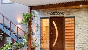 Una entrada de edificio moderno con un letrero que dice 'Welcome', una puerta de madera con un recorte en forma de luna creciente y una escalera a la izquierda.