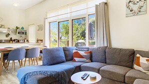 Een moderne woonkamer met een hoekbank, een kleine ronde tafel en een eetgedeelte met stoelen.