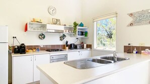 Een moderne keuken met witte kastjes, een roestvrijstalen spoelbak, een magnetron en een gasfornuis. Er is een raam dat natuurlijk licht binnenlaat en een decoratief bord aan de muur.