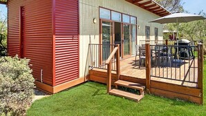 Een modern huis met een rode gevel, een grote schuifpui en een houten terras met tuinmeubilair.