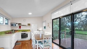 A modern kitchen with white cabinets, a microwave, and a dining area with white chairs. - Island Haven Villa Ramada Resort (Cowes)