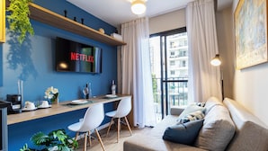 A modern living room with a flat-screen TV, a sofa, a dining area with chairs, and a large window with curtains. - Piscina-AC-Academia-Brazilian Corner (São Paulo)
