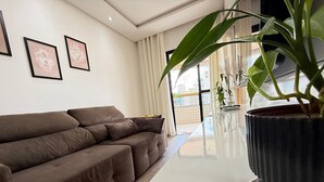 Een moderne woonkamer met een bruine bank, kunstwerken in lijsten aan de muur en een grote potplant.