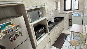 Een keuken met een koelkast, magnetron, fornuis, oven en een eettafel met twee stoelen.