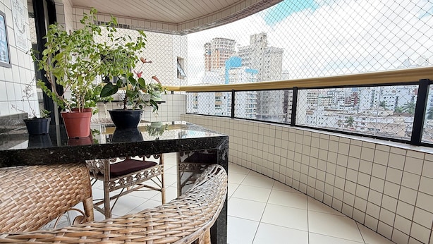 Een balkon met rieten meubilair, bloempotten en een uitzicht op stadsgebouwen.