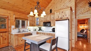 Una cocina tipo cabaña de madera con una isla central, armarios de madera, un refrigerador y un comedor con una silla.