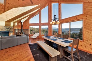 Un amplio salón con chimenea, una mesa de comedor con sillas y grandes ventanales con vistas a la montaña.