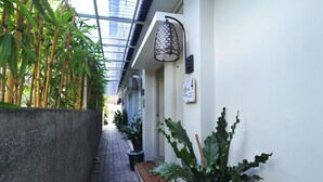 A narrow corridor with a concrete wall on one side and a row of potted plants on the other. There is a sign indicating the floor level and a metal lamp post. - Dasinem Family Homestay (Pogung Lor)