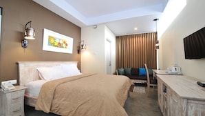A hotel room with a bed, bedside table with a phone, a desk with a kettle, a TV, and a painting on the wall. - Dasinem Family Homestay (Pogung Lor)
