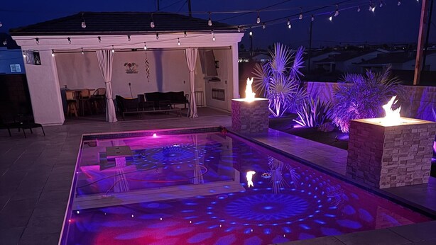 Una piscina con un diseño luminoso geométrico, una zona de estar cubierta y un hogar.