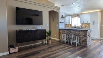 Un salon moderne avec un grand canapé en cuir noir, un téléviseur à écran plat fixé au mur et un ventilateur de plafond.