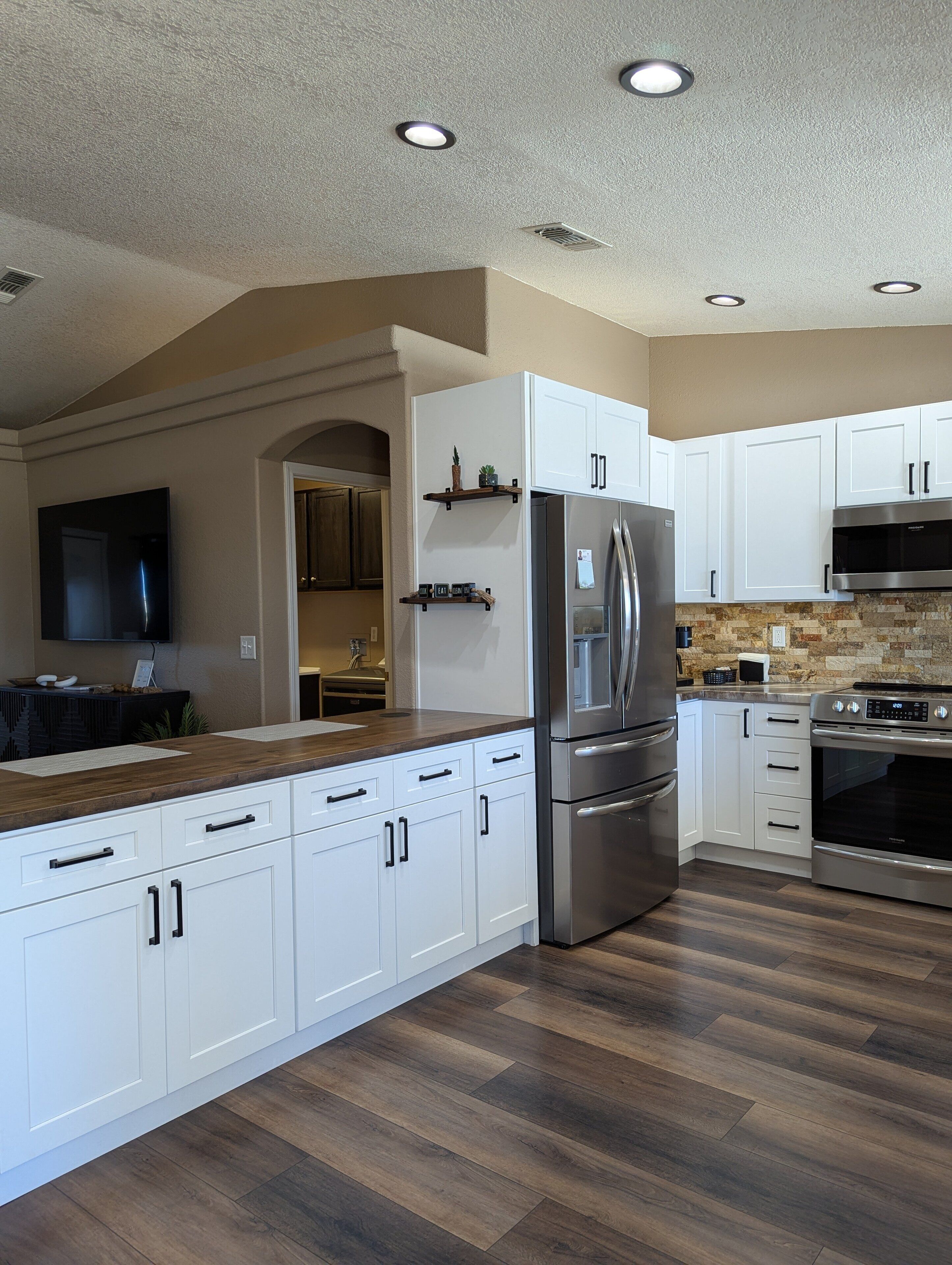 Une cuisine moderne avec des meubles blancs, des appareils en acier inoxydable et un parquet en bois disposé en chevrons.