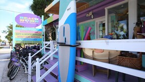 A colorful beach-themed storefront with a sign listing rentals like kayaks, golf carts, and bikes.