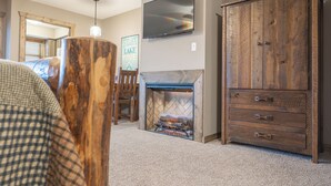 A living room with a fireplace, a television mounted on the wall, and a large wooden cabinet. - Studio Style, Near Table Rock Lake- Ticket Deals & Resort Perks! (Branson)