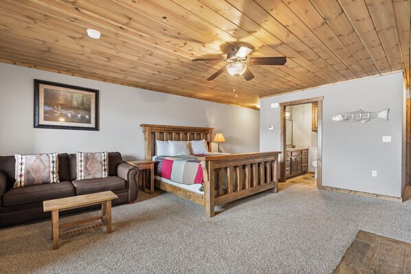 A cozy bedroom with a wooden ceiling, a bed with a wooden headboard, a brown sofa, and a small wooden table. - Lakefront, Sleeps 8. Enjoy Resort Amenities and Exclusive Ticket Deals (Branson)