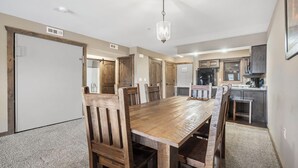 A dining area with a wooden table and chairs, a chandelier, and a kitchen in the background. - 1 BDRM, Lake Community Condo near Silver Dollar City!  Ticket Deals and Resort Perks (Branson)