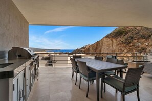 An outdoor patio with a grill, dining table, and chairs, overlooking a rocky landscape and the sea. - Ocean View, 2 Infinity Pools, Pedregal, 3 King bed (Cabo San Lucas)