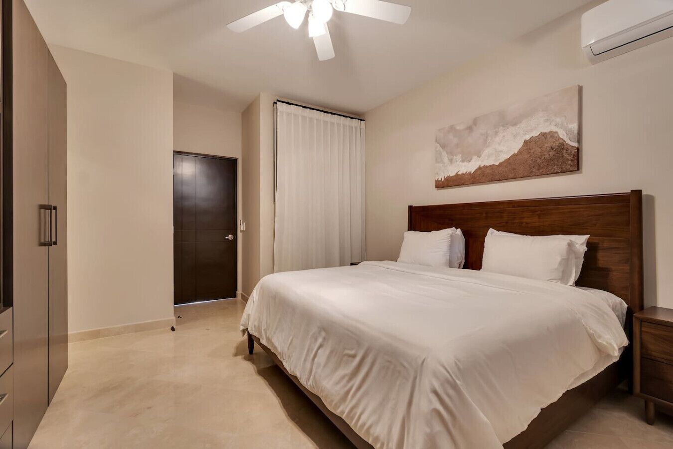 Ein modernes Hotelzimmer mit einem großen Bett, einem Holzkopfschild, einem Deckenventilator und einem Bild an der Wand.