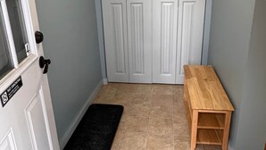 Un pasillo con una puerta cerrada, un banco de madera y un felpudo negro.
