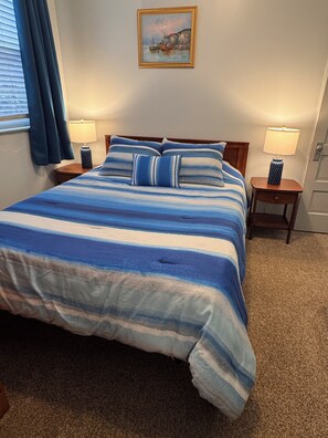 A bedroom with a bed, two bedside tables with lamps, a painting on the wall, and a window with curtains.