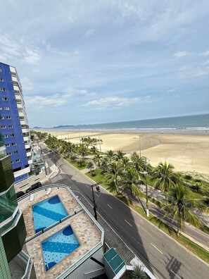 A high-rise building with a rooftop pool area and a view of a beach. - Pé na Areia Praia do Maracanã II (Praia Grande)