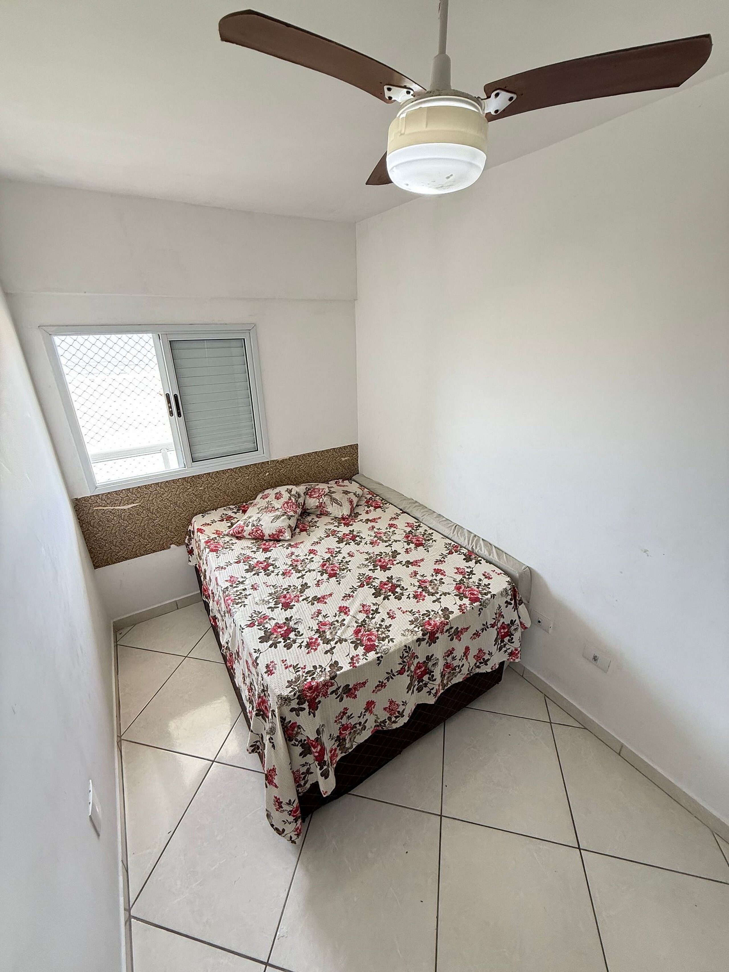 A bedroom with a bed, a ceiling fan, a window with blinds, and a tiled floor.