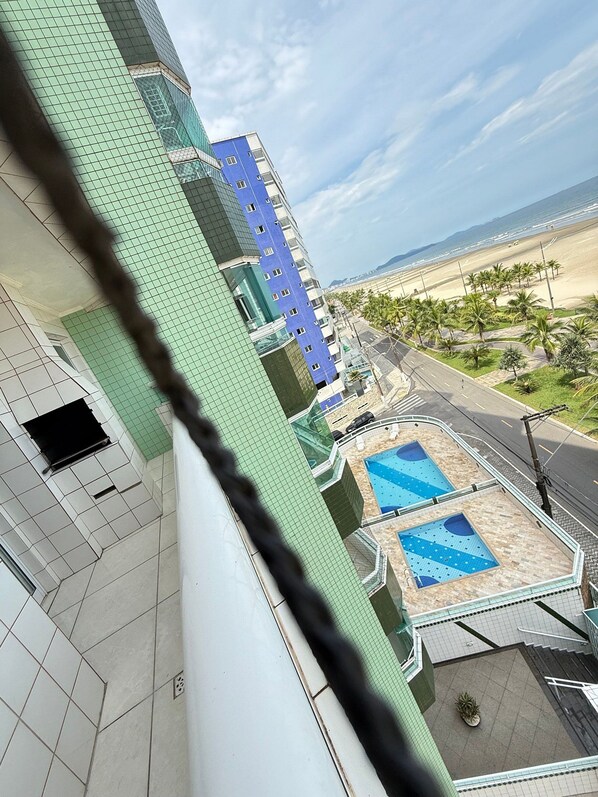 A high-rise building with a pool area, a beach view, and a clear sky.