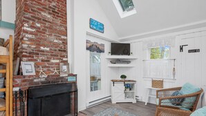 Ein gemütliches Wohnzimmer mit Kamin, Fernseher, Korbmöbeln und Blick ins Freie.