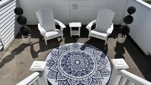Eine Terrasse mit zwei weißen Adirondack-Stühlen, einem kleinen Tisch und einem dekorativen Mandala-Teppich.