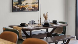 Une table à manger dressée avec des bols noirs, des verres transparents et une bougie, agrémentée d’un set de table en fibres tressées et d’un tableau accroché au-dessus.