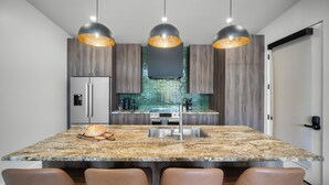 Une cuisine moderne dotée d’un îlot en granit, d’appareils électroménagers en acier inoxydable et de luminaires suspendus.