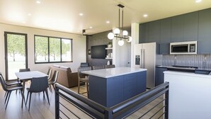 A modern kitchen with a central island, built-in appliances, and a dining area with a view of trees. - Experience Elegance at the Montclair in Our Luxury Villa (Springdale)