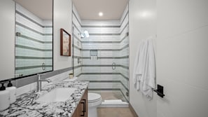 A modern bathroom with a marble sink, a glass shower enclosure, and a white toilet.