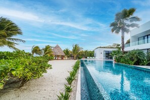 A resort pool area with a clear view of the ocean, a thatched hut, and modern buildings. - Upscale 5-bed Beachfront Villa w/ pool , pier & ocean front (Placencia)