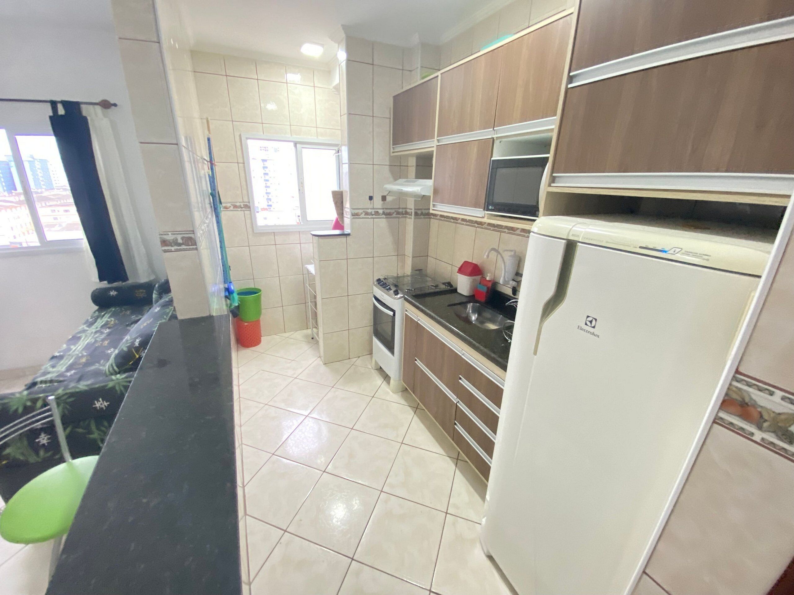 A compact kitchen with a refrigerator, stove, microwave, and a window.
