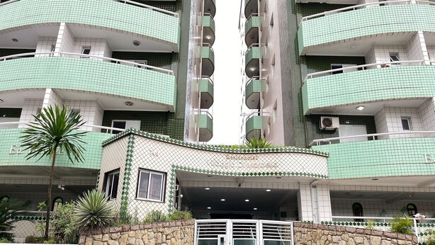 A multi-story residential building with a stone facade, green-tiled balconies, and a central entrance with a staircase. - Pé Na Areia Praia da Ocean II (Praia Grande)