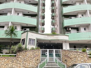 A multi-story residential building with a stone facade, green-tiled balconies, and a central entrance with a staircase. - Pé Na Areia Praia da Ocean II (Praia Grande)