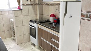 A kitchen with wooden cabinets, a stove, a microwave, and a refrigerator. - Pé Na Areia Praia da Ocean II (Praia Grande)