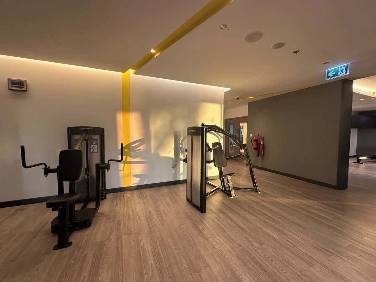 Un gimnasio con equipamiento de ejercicio, piso de madera y una pared de acento amarilla.