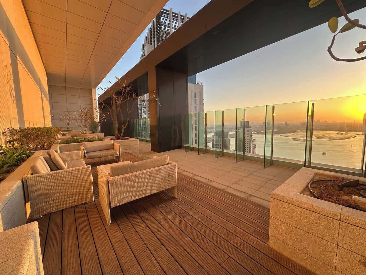 A rooftop terrace with wicker furniture and a view of the cityscape at sunset.
