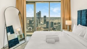 A hotel room with a large bed, a mirror, a nightstand, and a view of a cityscape through large windows. - Burj Royale Dubai Downtown (Dubai)