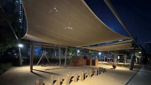 An outdoor play area with a sandy surface, wooden play structures, and a canopy providing shade. - Burj Royale Dubai Downtown (Dubai)