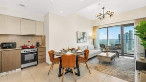 A modern apartment with a kitchen, dining area, and living room. It features a large window, a dining table with chairs, a sofa, and a coffee table. - Burj Royale Dubai Downtown (Dubai)