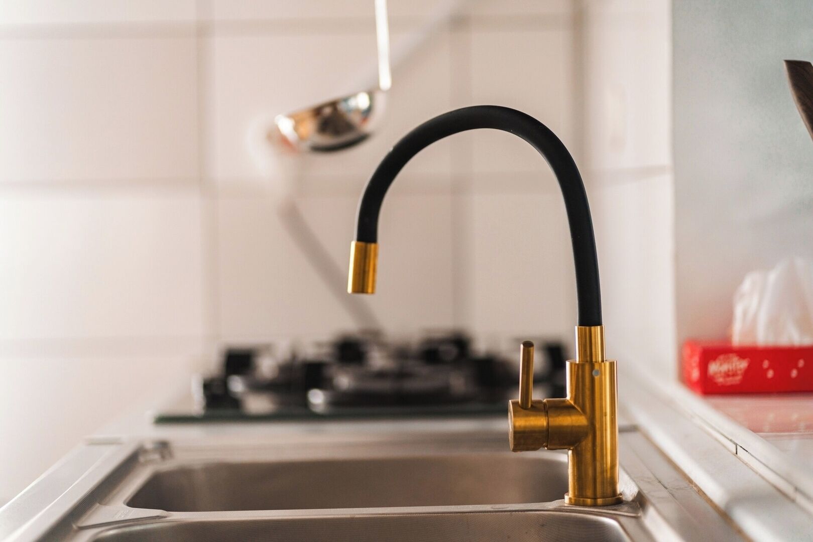 Un évier de cuisine avec un robinet moderne, une cuisinière et une boîte rouge en arrière-plan.